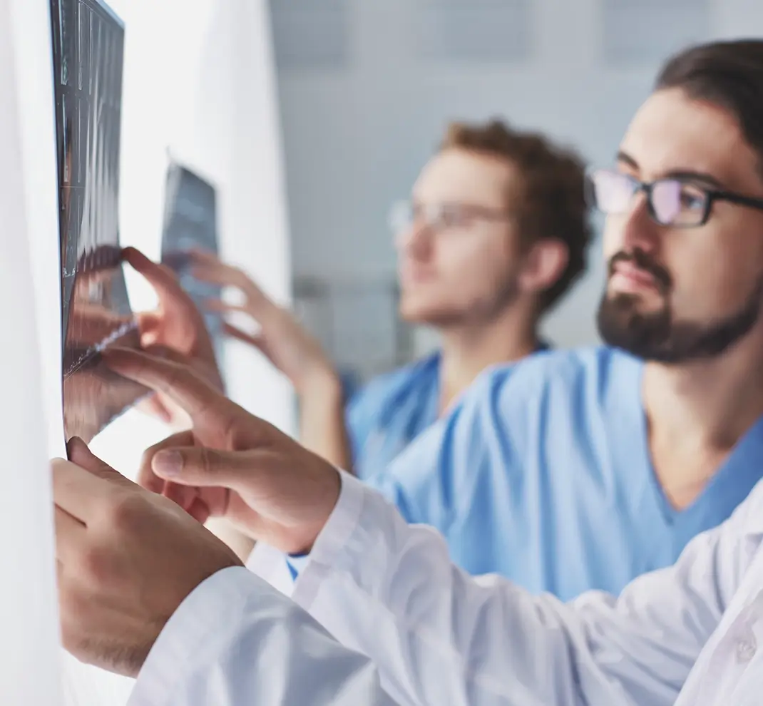 Ein medizinisches Team analysiert gemeinsam radiologische Aufnahmen (Röntgenbilder oder CT) an einer Lichtwand.