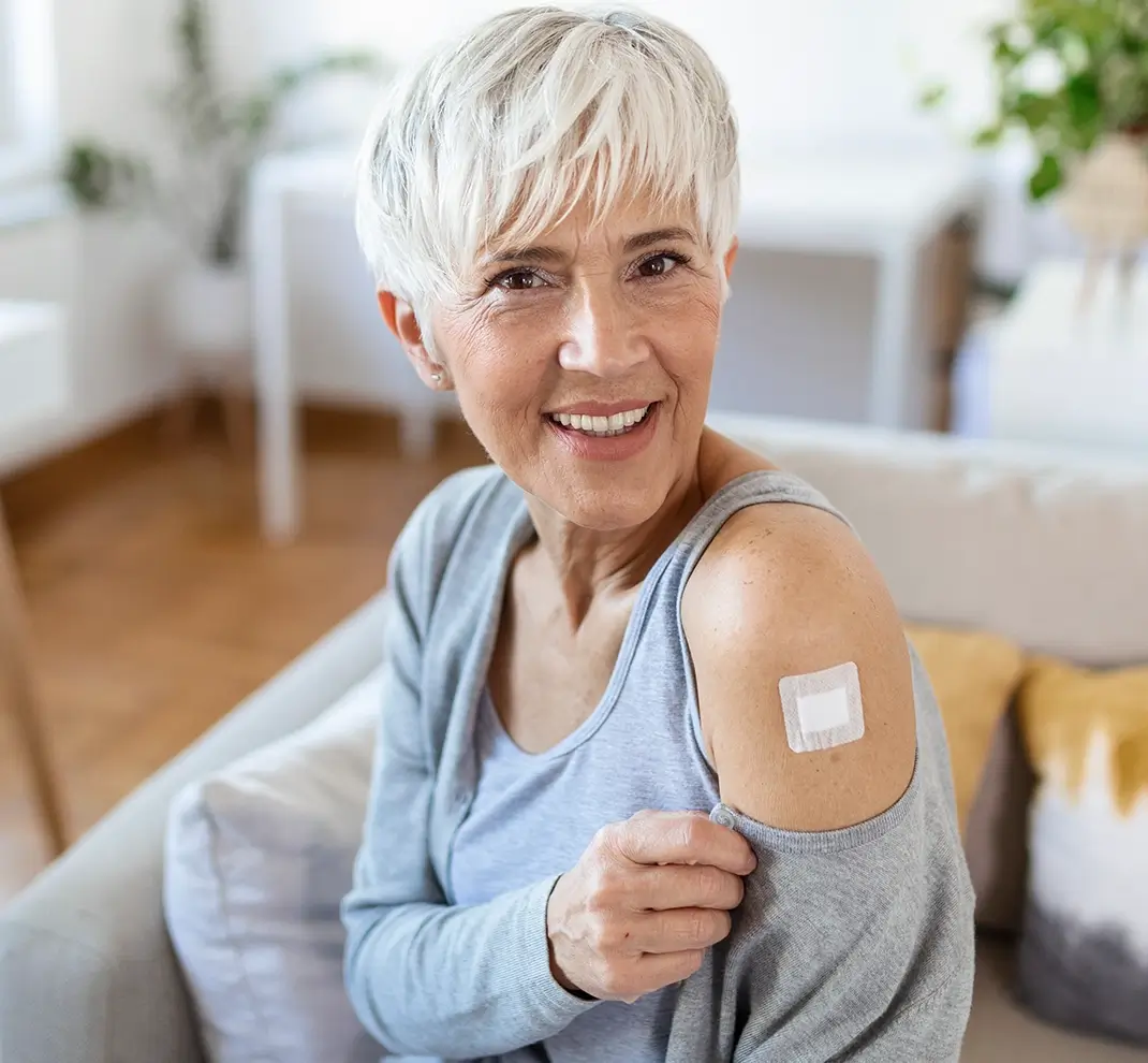 Eine lächelnde ältere Patientin zeigt ein Pflaster auf ihrem Oberarm nach einer Impfung oder Allergie-Spritzenkur.