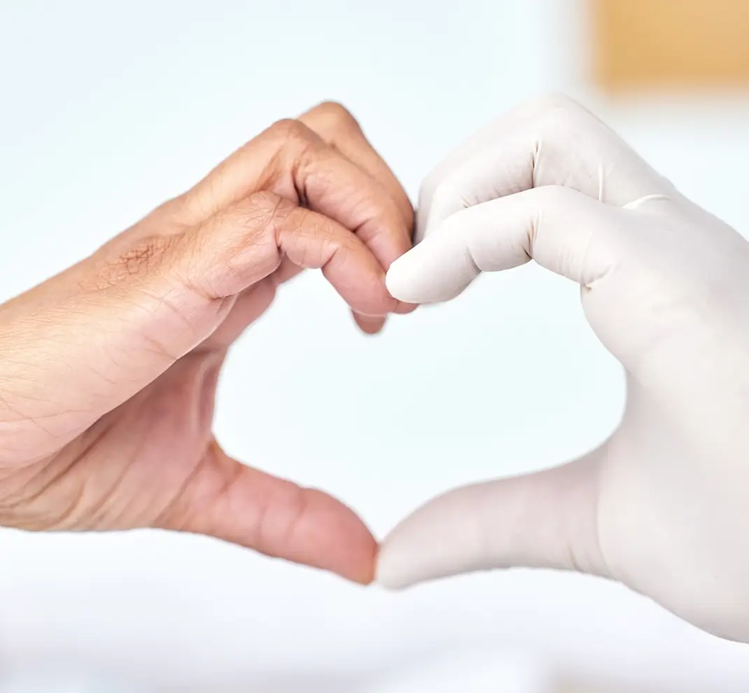 Ein Patient und eine medizinische Fachkraft mit Handschuh formen gemeinsam ein Herz mit ihren Händen in der HNO-Praxis Festner.